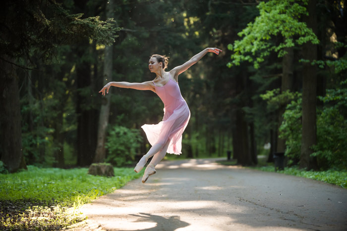 ballet dancer jumping on road through wooded forest