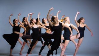 group of young adult ballerinas wearing black posing on stage